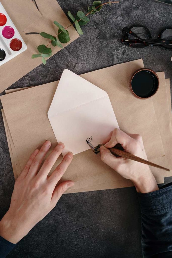 A heart being drawn on to an envelope which rests on brown blank writing paper. 