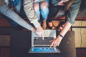 Three people from above pointing at a site with ways to make friends online on their laptop