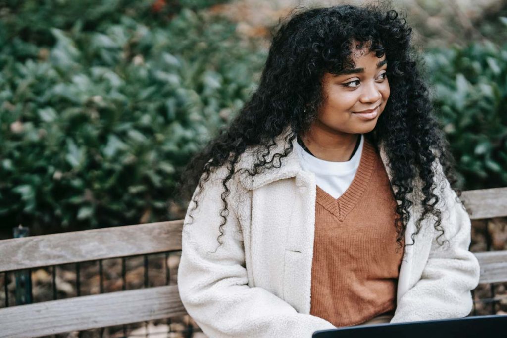 A woman sits on a bench typing and smiles