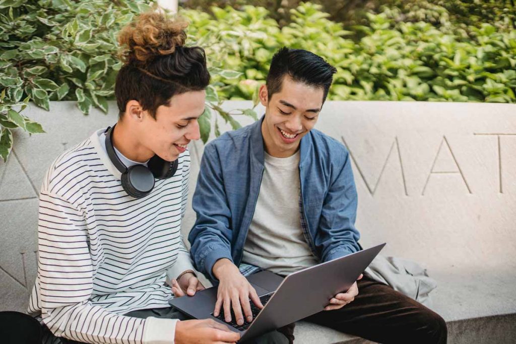 Two men sit writing a pen pal a conversation starter on a laptop