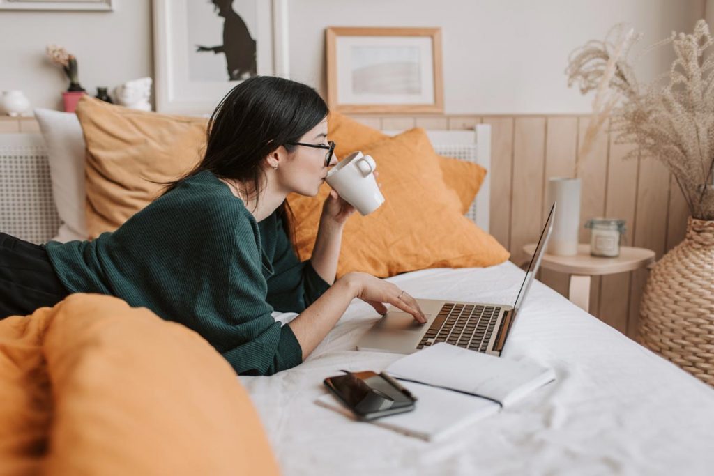 A woman practices different ways to learn a language while lying on her bed with a laptop