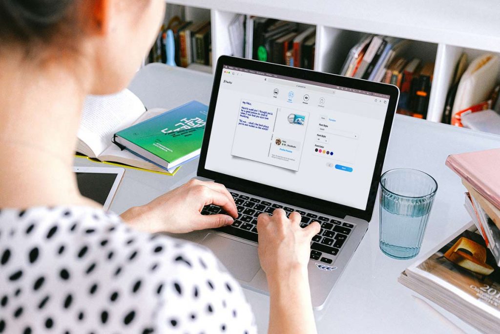 A laptop where a woman is writing a postcard as she becomes a pen pal 