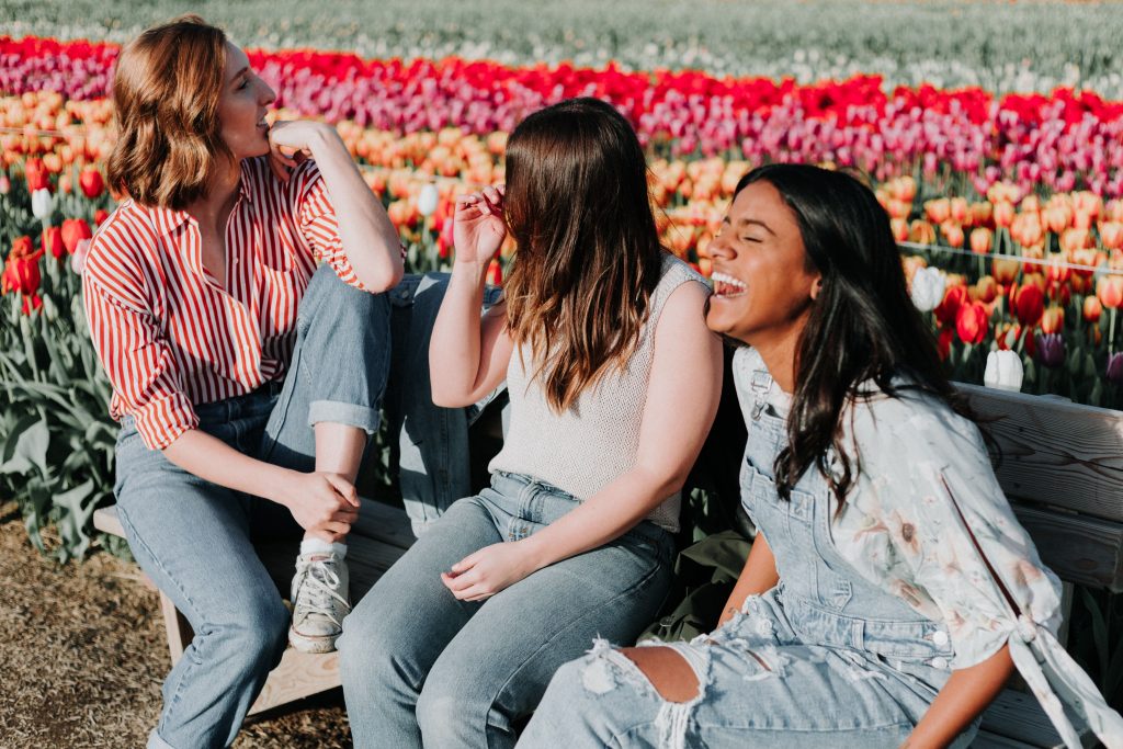 friends sitting on a bench in front of a flower field laughing