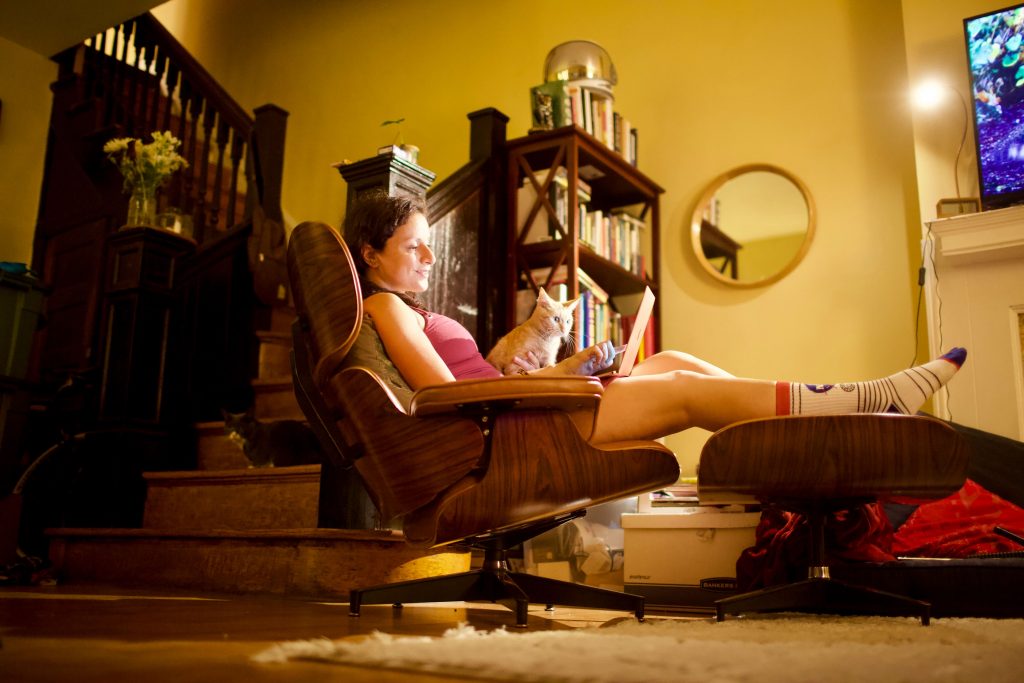 Girl sitting in her room with a laptop and a cat on her legs.