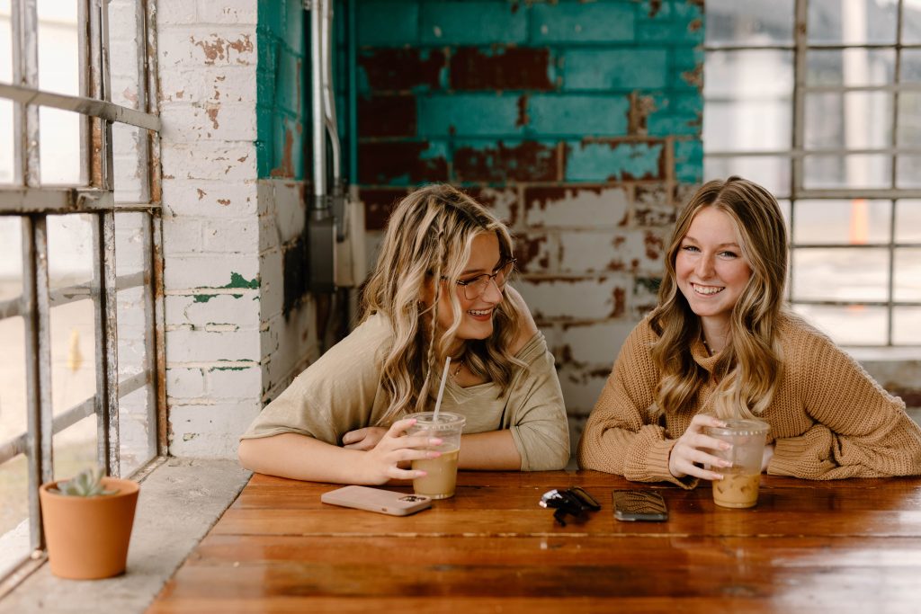 Two friends with blonde hair sitting in a cafe and laughing.